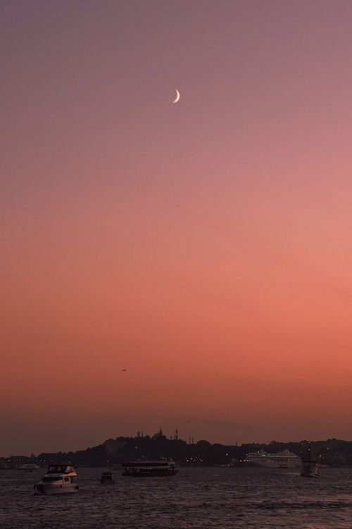Free Crescent moon over cityscape with boats on water at dusk. Perfect for serene evening scenes. Stock Photo