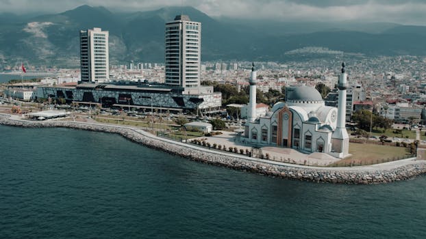 Aerial photograph showcasing İskenderun's mosque and cityscape against the mountainous backdrop on a sunny day.
