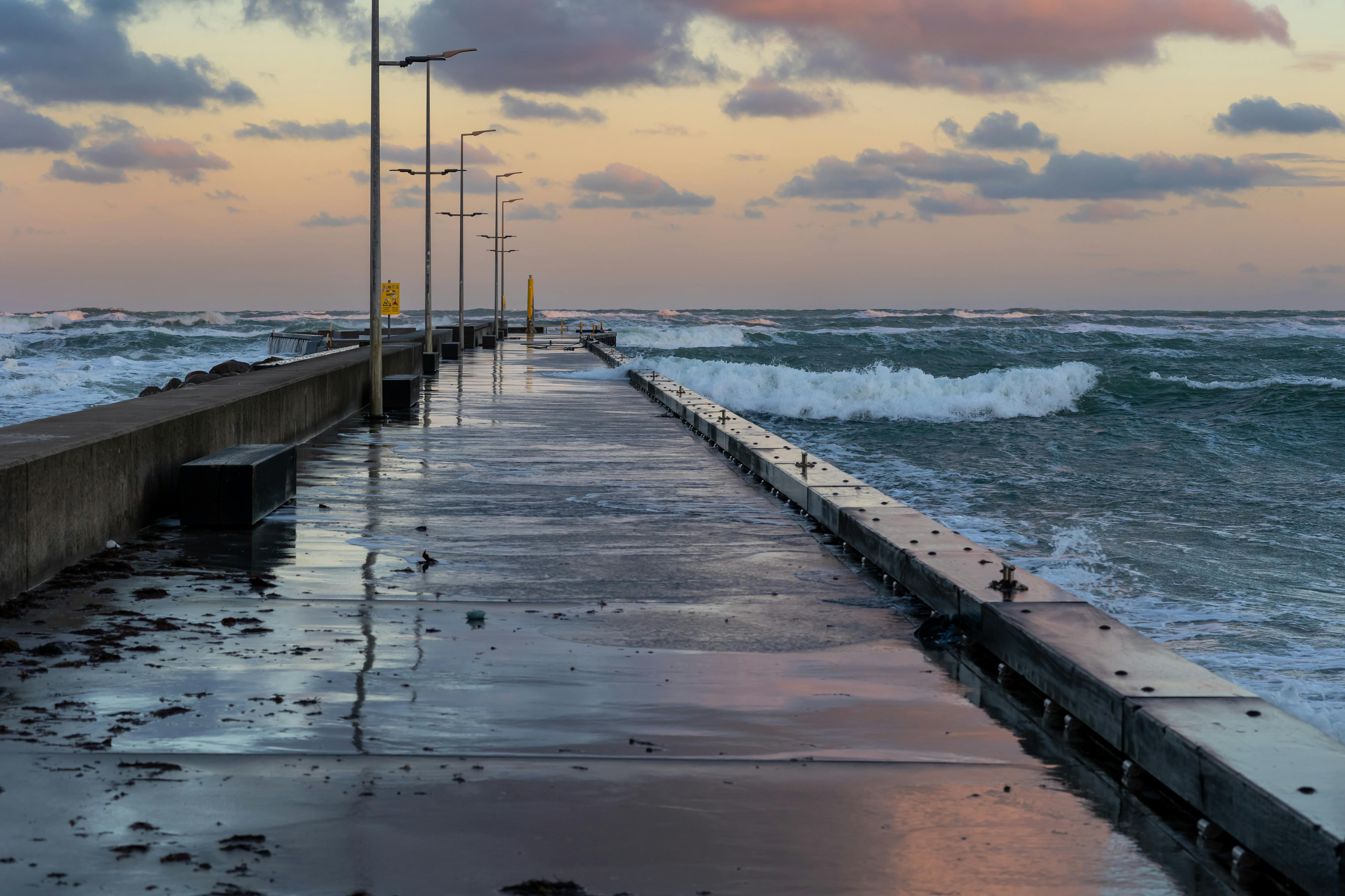Calm sunset over Løkken pier with waves crashing against the shore.