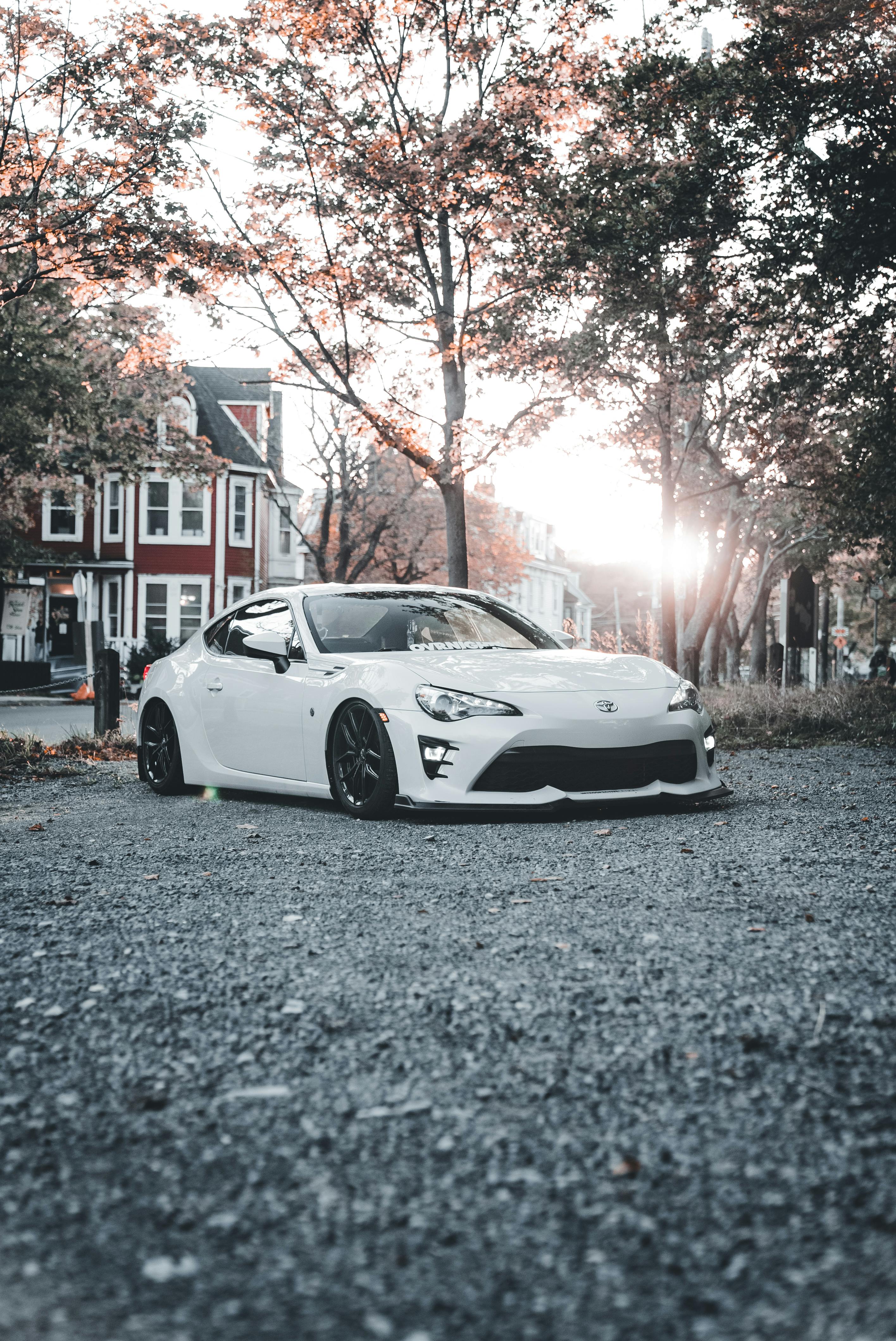 Free Stylish white car parked outdoors with autumn foliage and soft sunlight. Stock Photo