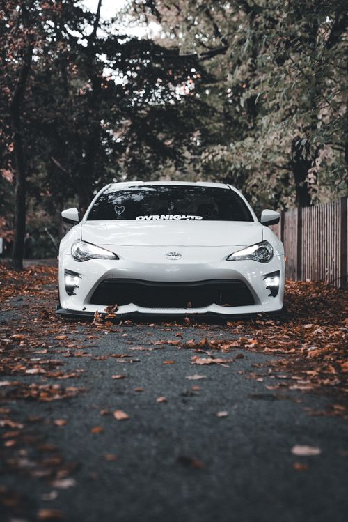 Free Sleek white sports car on a picturesque fall road with fallen leaves. Stock Photo