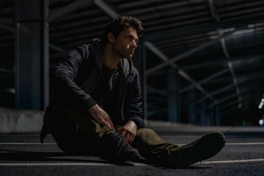 Thoughtful man sitting under a bridge at night, deep in reflection.