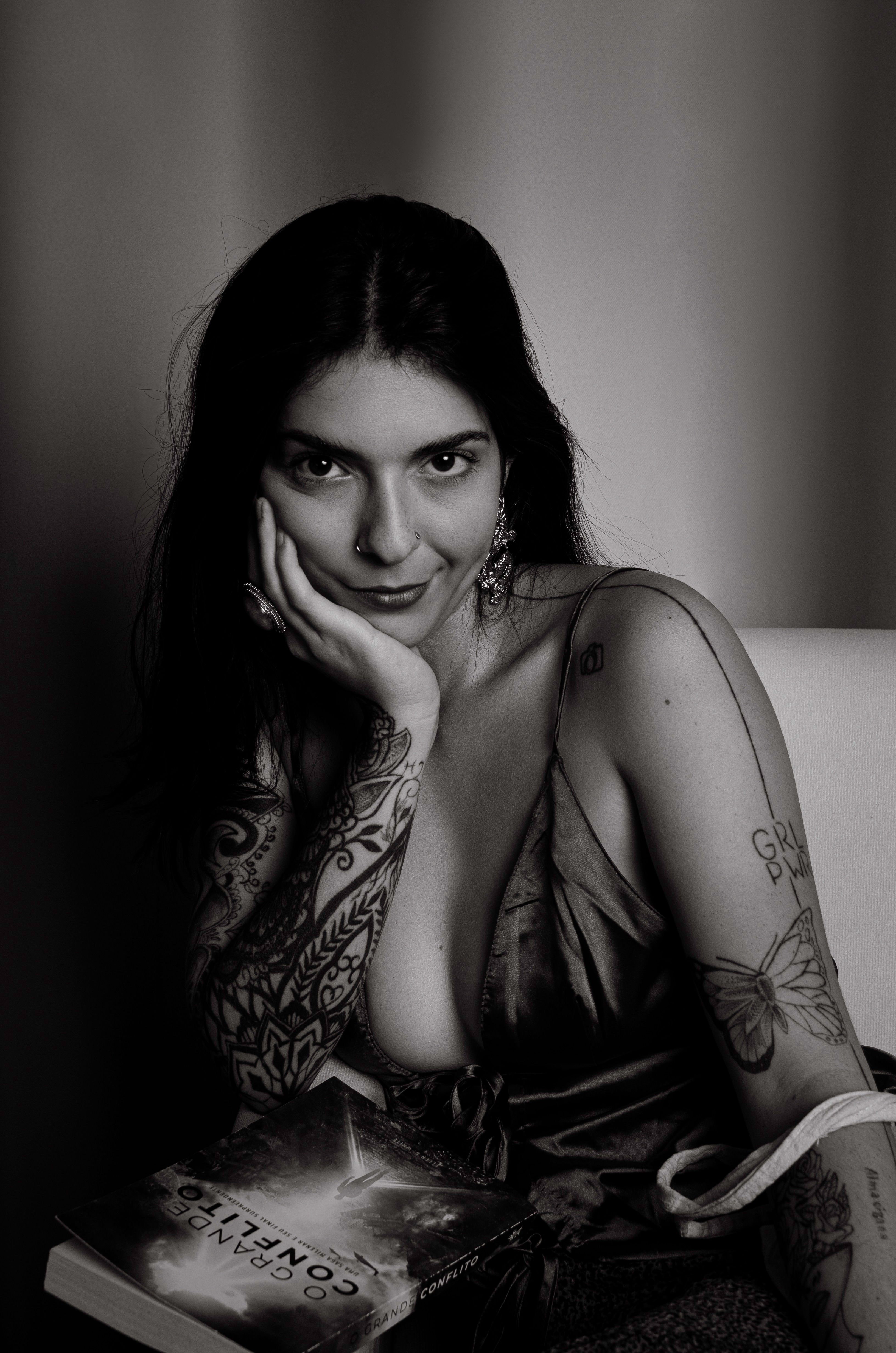 Artistic black and white photo of a tattooed woman posing with a book.