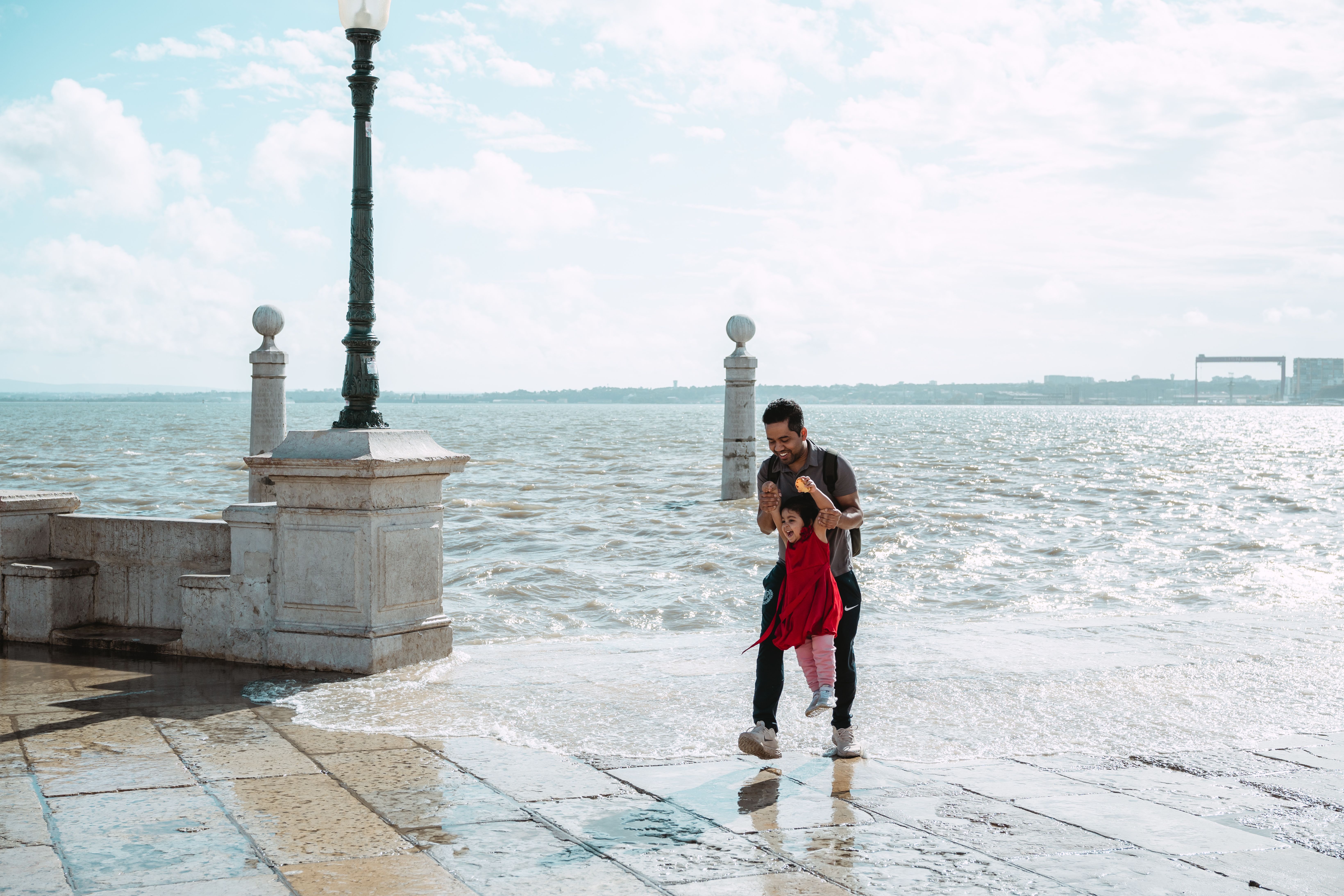 Father and daughter enjoy a playful moment by the waterfront on a sunny day.
