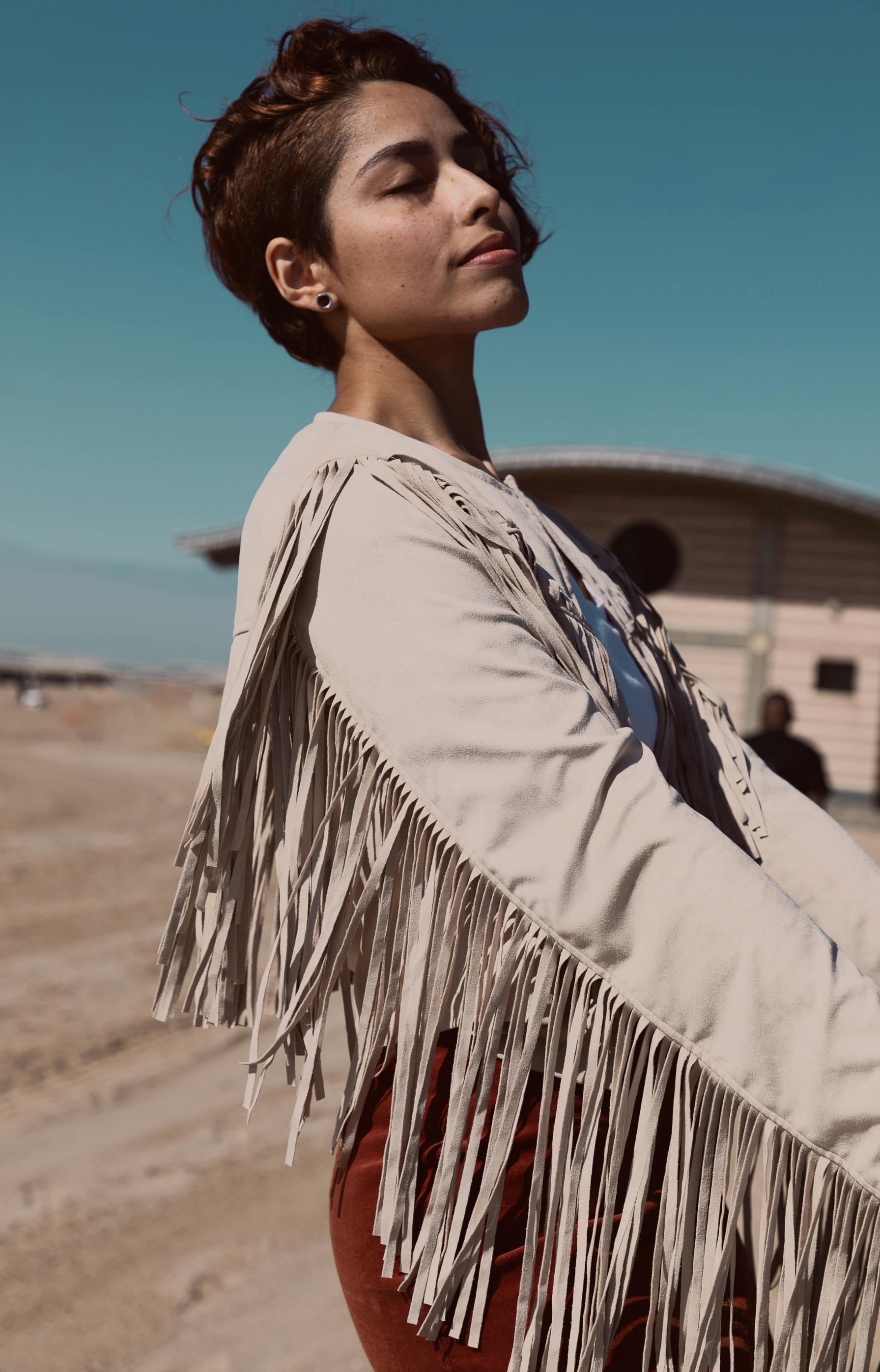 一张女子侧身图，她留着短发，闭着眼睛，在户外穿着一件刘海夹克