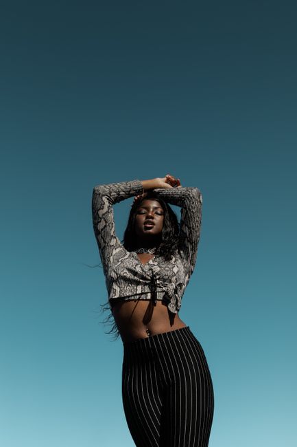Elegant portrait of a fashionable black woman posing outdoors against a clear sky.