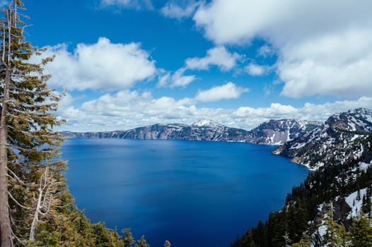 在多云的天空下，火山口湖的全景令人惊叹，清澈的蓝色海水与白雪皑皑的山脉相映成趣