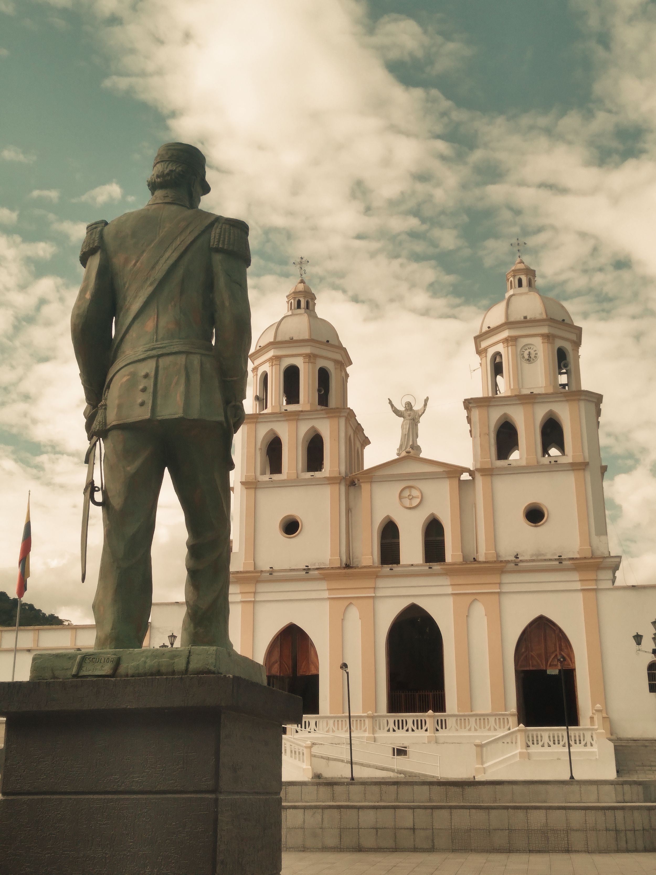 A grand church with a prominent statue in the foreground under a vibrant sky.