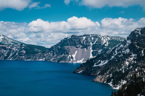 Free Capture the breathtaking scene of Crater Lake surrounded by majestic snow-capped mountains under a vibrant sky. Stock Photo