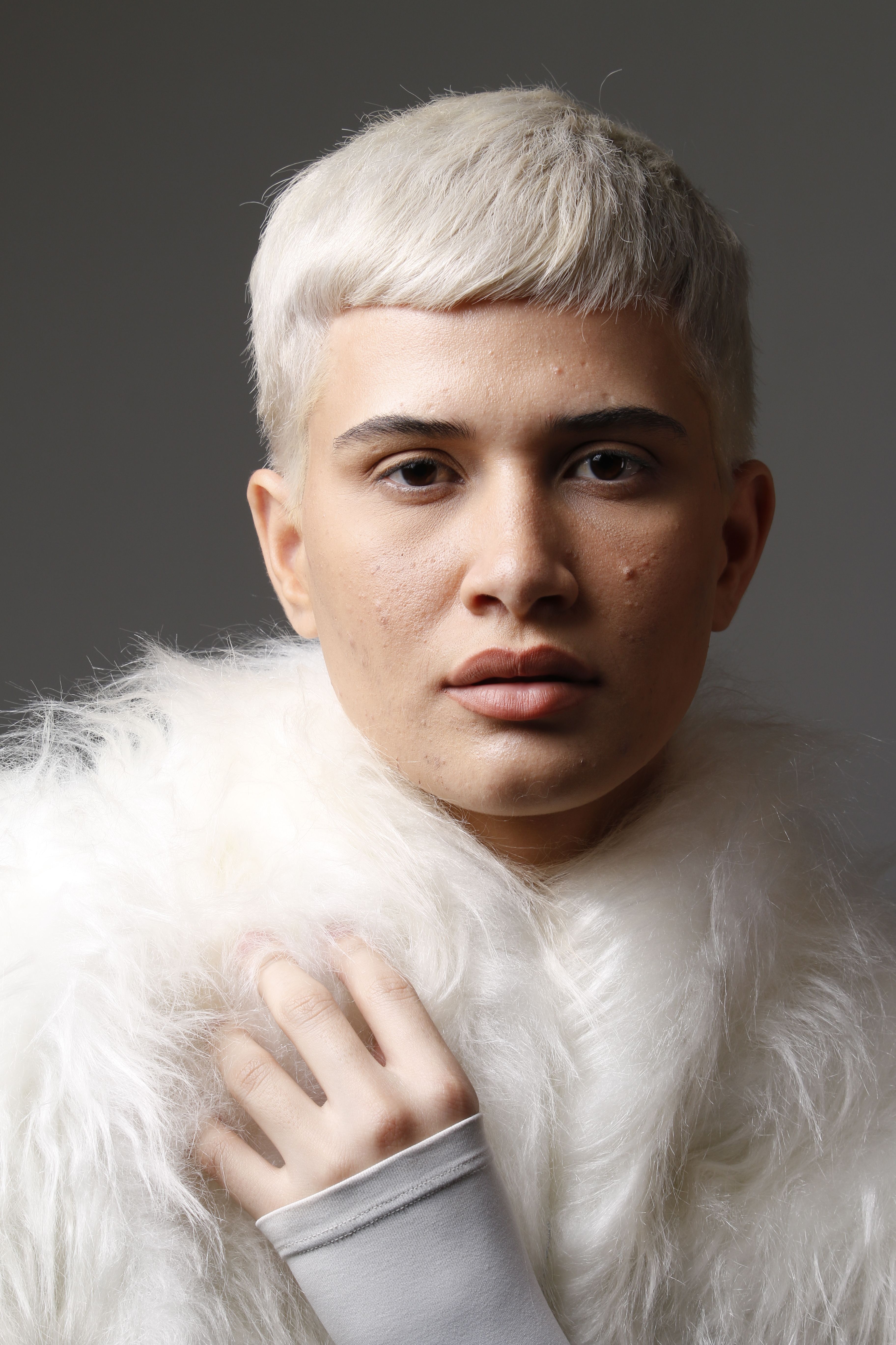 Close-up portrait of a stylish young adult wearing a white fur coat.