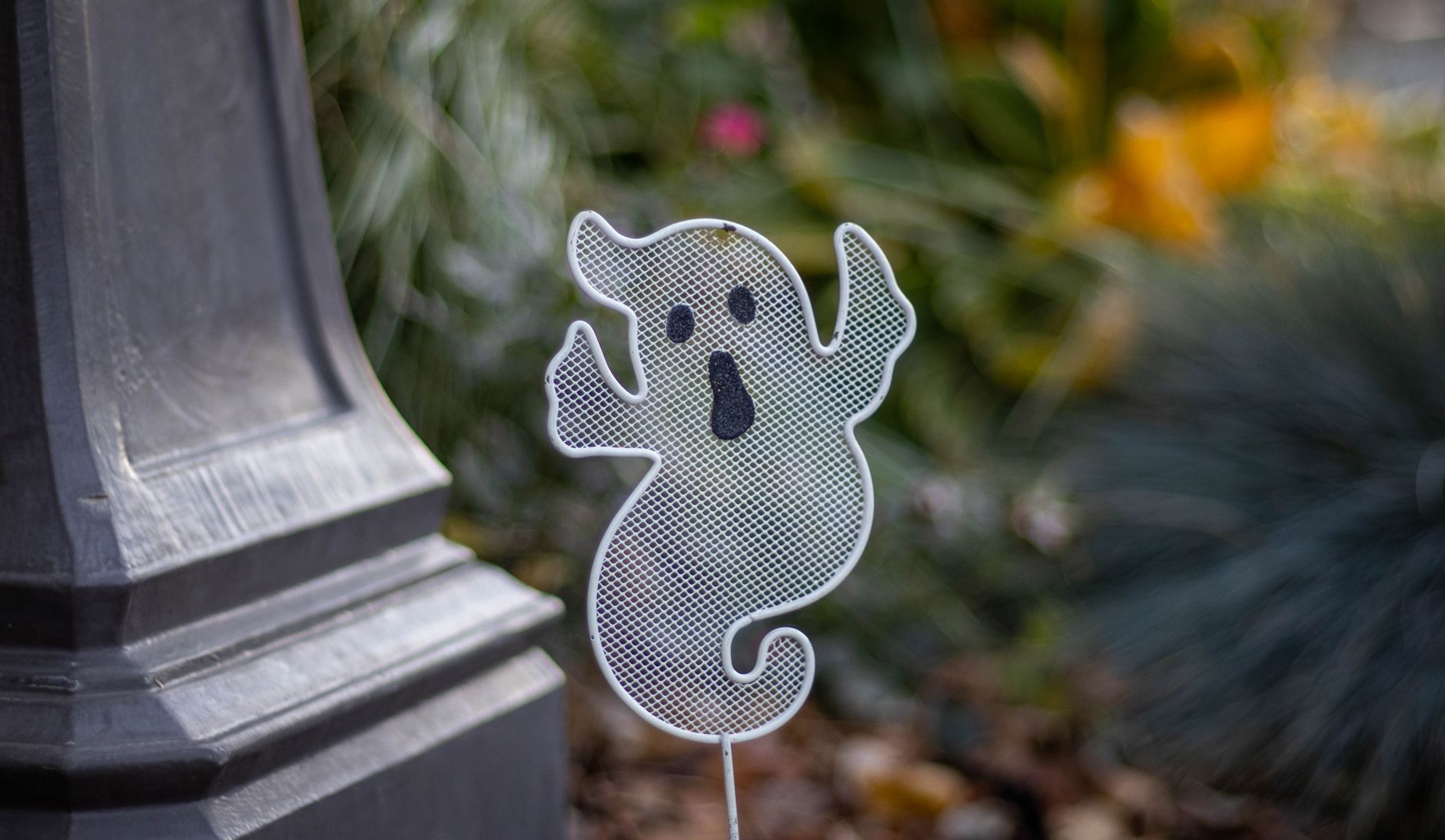 A spooky ghost decoration beside a garden post, perfect for Halloween themes.