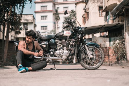 Free A man rests next to a classic Royal Enfield motorcycle in an urban setting. Stock Photo