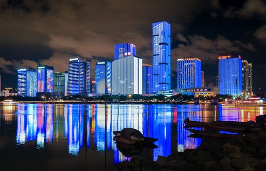 Stunning city skyline with illuminated skyscrapers reflecting in a calm river under a night sky.