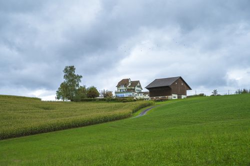 Free Picturesque farmhouse and barn amidst lush greenery and cloudy sky. Stock Photo