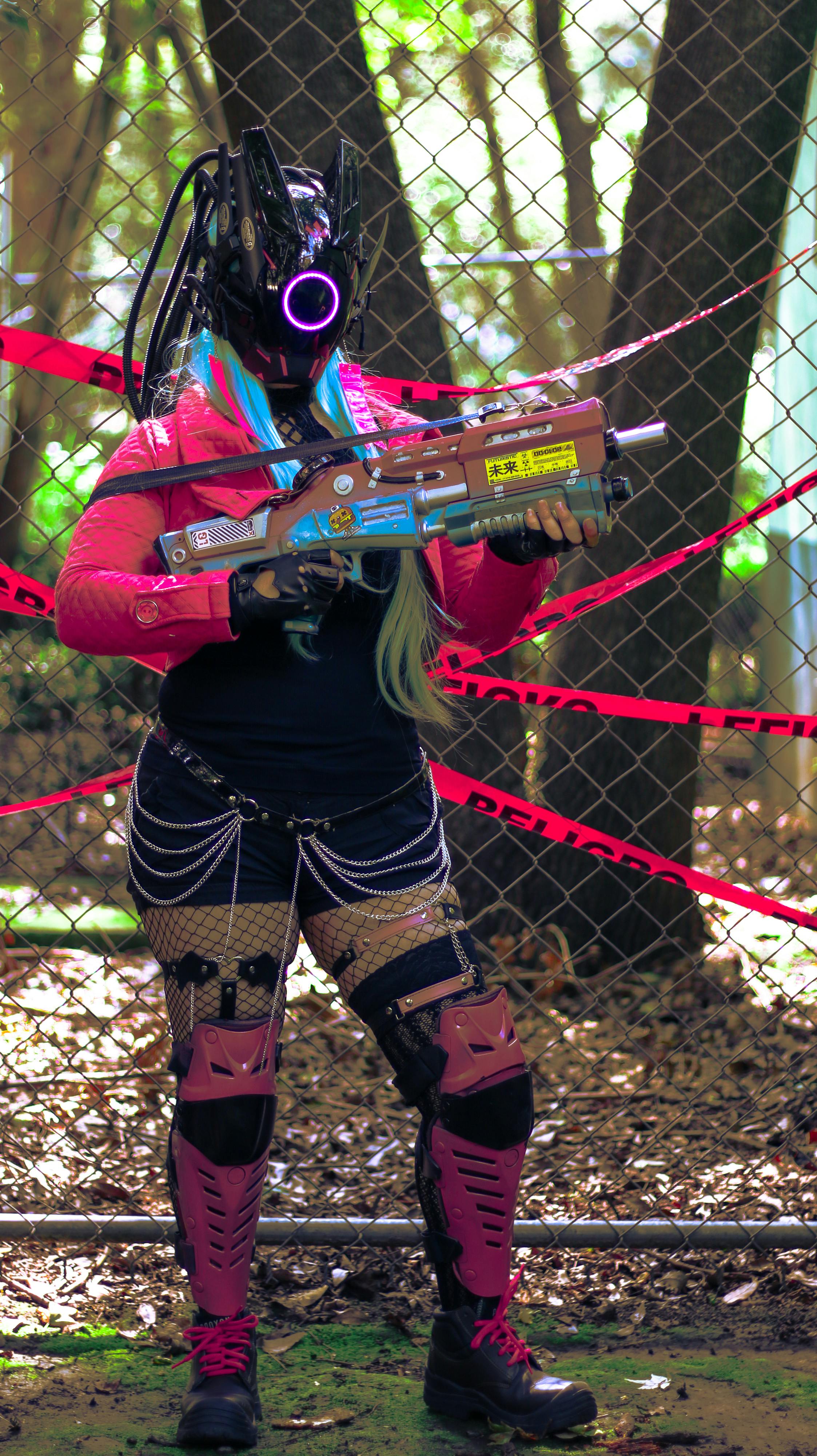 A cosplayer in cyberpunk attire with neon elements holds a sci-fi weapon outdoors.