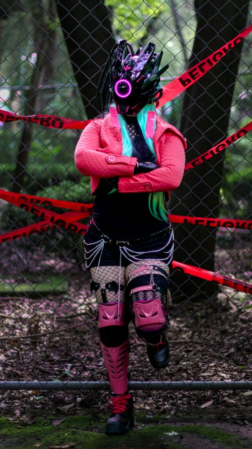 Free A person in cyberpunk attire stands confidently in a forest setting, creating a striking contrast. Stock Photo