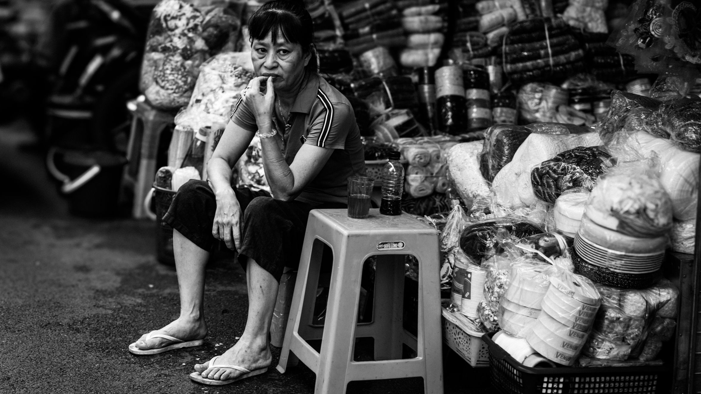 Street vendor sitting among goods in a Hanoi market, Vietnam, showcasing local commerce and lifestyle.
