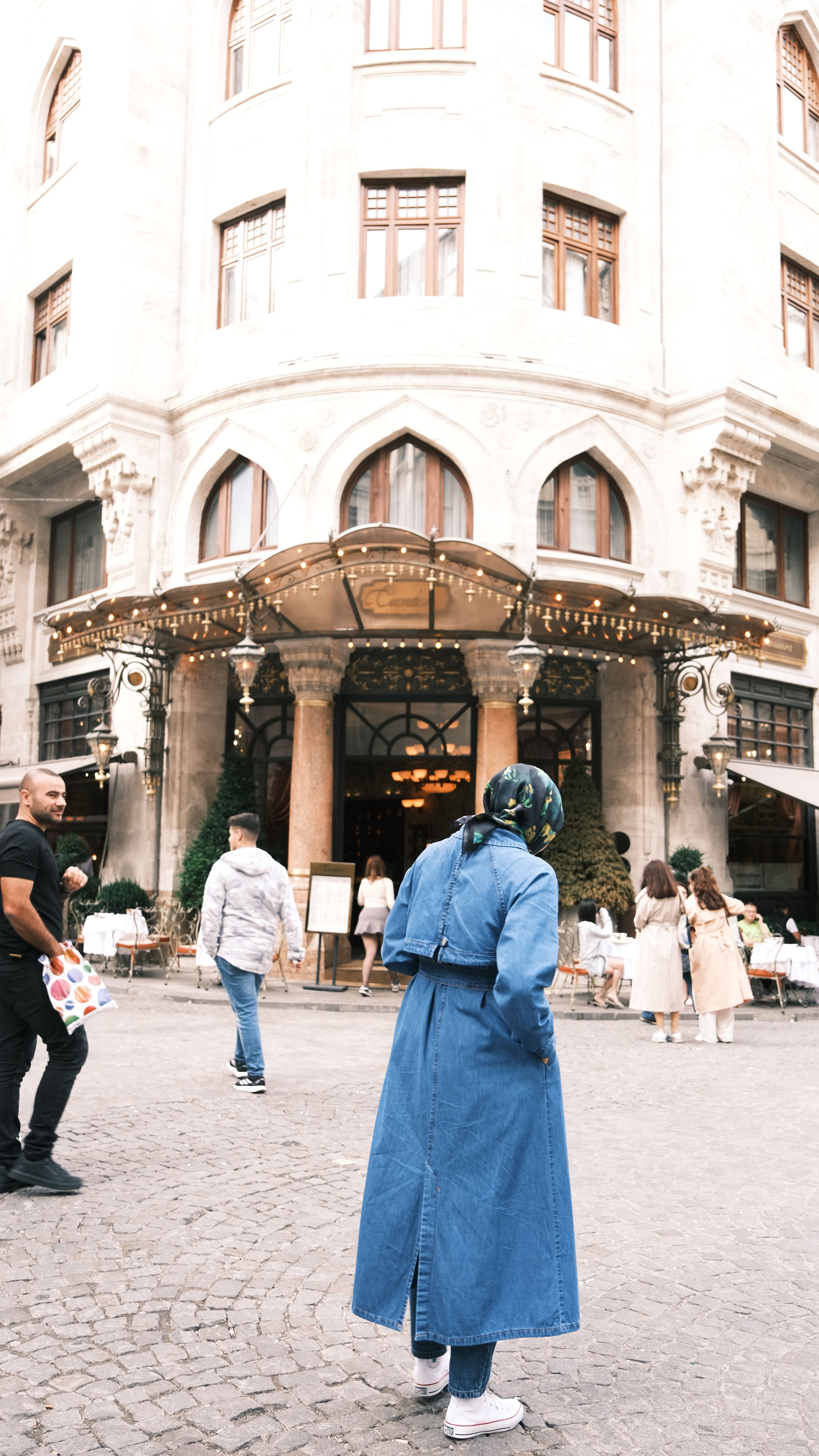 People walking outside a grand historic building with a decorated entrance in a busy street.