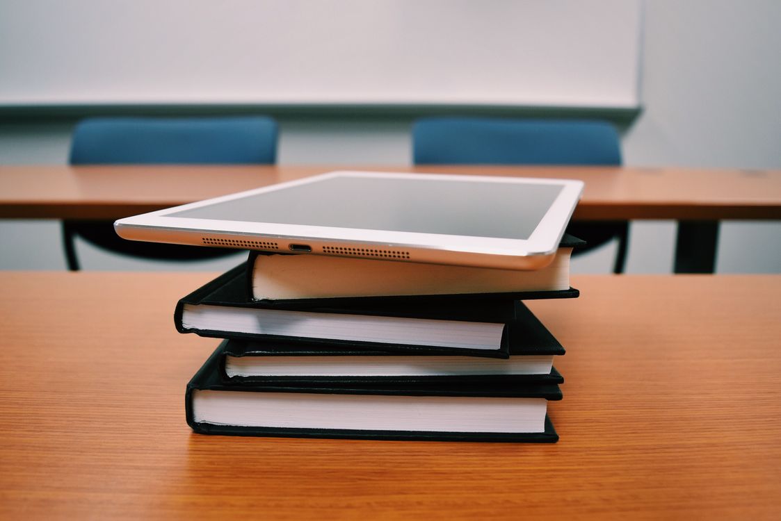 Free A tablet rests on top of a stack of books in an empty classroom, illustrating modern education. Stock Photo