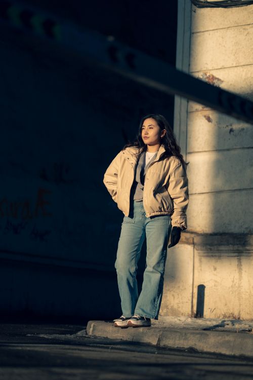 Free A woman stands in a shadowed urban setting during twilight, wearing casual attire. Stock Photo