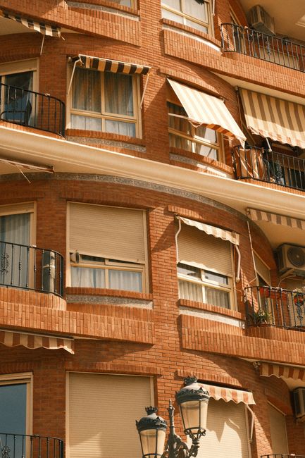 Close-up of a classic brick apartment building featuring striped awnings and wrought iron balconies.