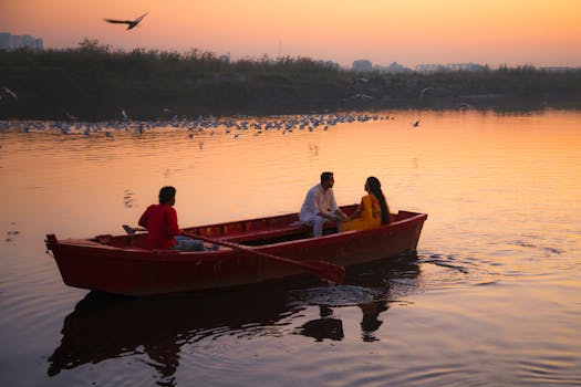 A tranquil scene of three people in a boat during sunrise with birds flying over a river in India.