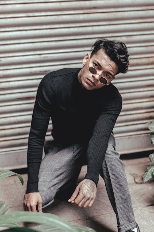 Foto De Hombre Con Camisa Negra De Manga Larga, Pantalón Gris Y Gafas De Sol En Cuclillas Posando