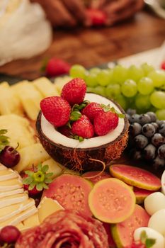 A vibrant tropical fruit platter featuring strawberries in a coconut shell among an array of fruits.