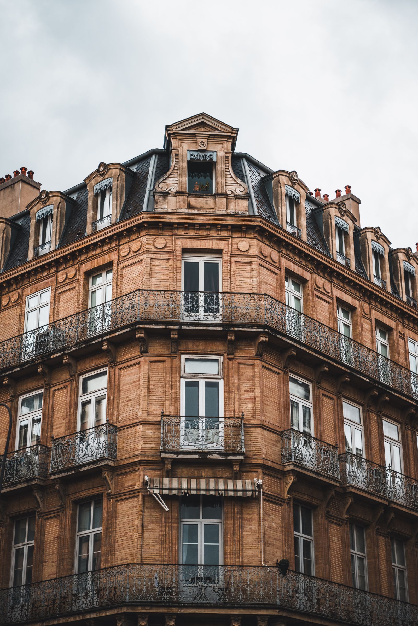 Immeuble d’angle en brique, Toulouse Immeuble ancien d’angle à Toulouse, façade de brique rouge, balcons en fer forgé et fenêtres à petits carreaux.