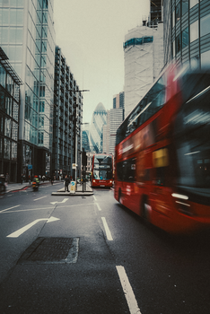 Busy London street scene with blurred red buses and modern architecture.