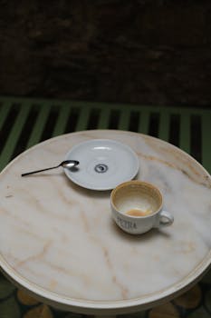 Empty espresso cup and saucer on a marble table with a spoon.