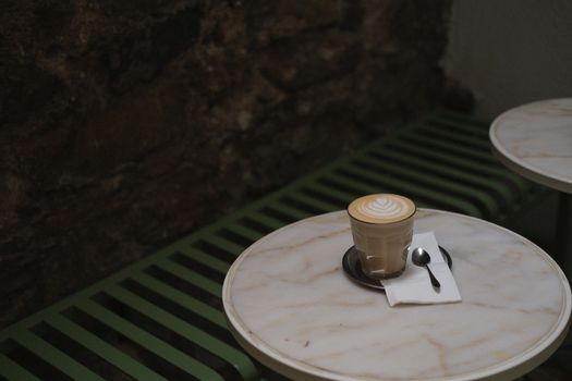A beautifully crafted latte with delicate latte art sits on a marble table in a cozy café setting. The ambient lighting enhances the warm atmosphere.