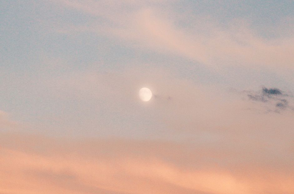 A calm evening sky featuring a full moon surrounded by gentle clouds and soft hues.