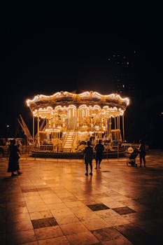 A brightly lit carousel in a Tiranë park with silhouettes of people around it at night.