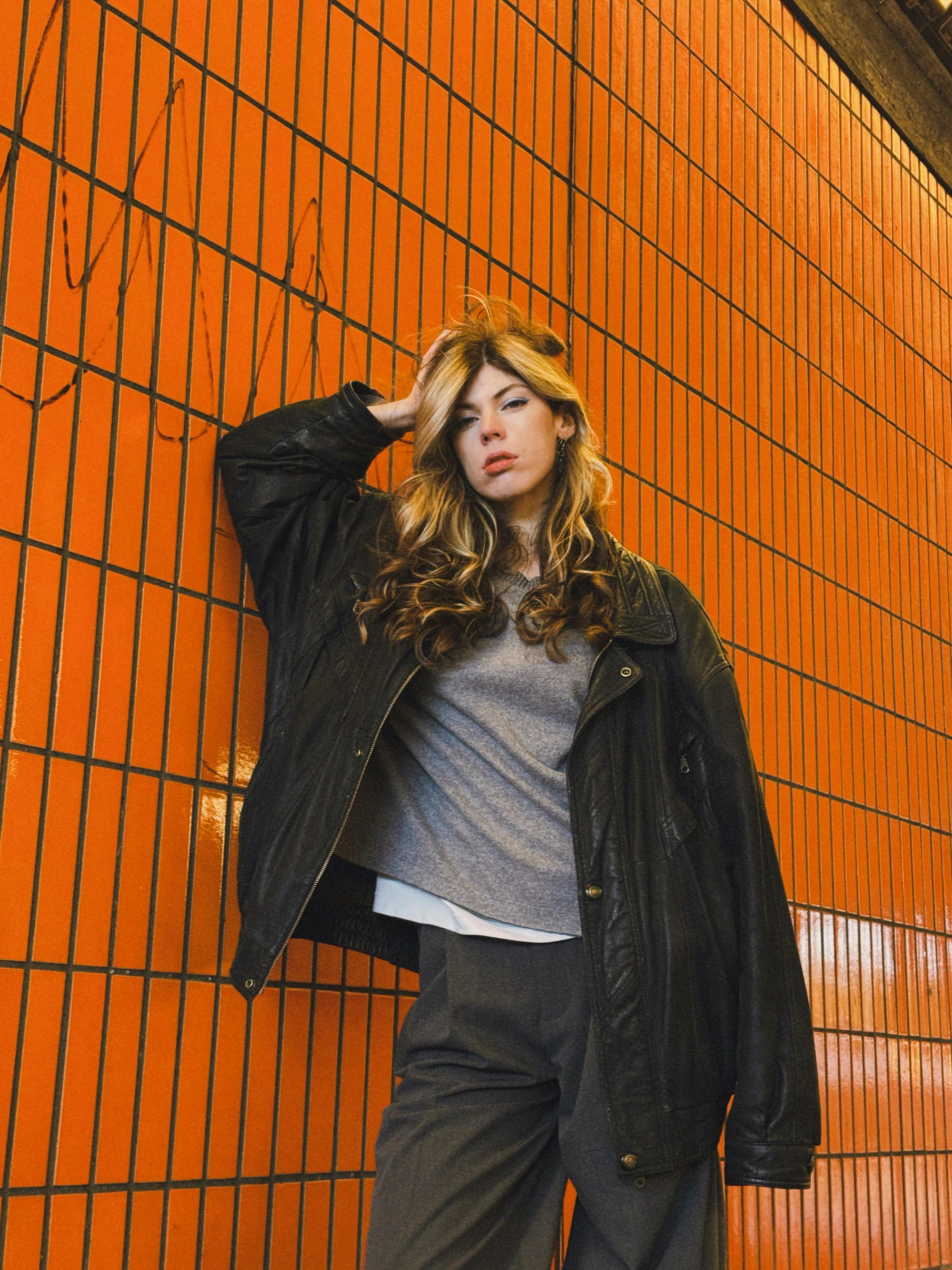 Stylish woman in casual wear posing confidently against an orange tiled wall in Berlin.