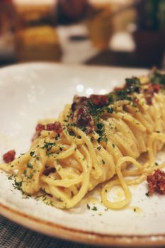 Close-up of creamy spaghetti carbonara with herbs and bacon garnish.