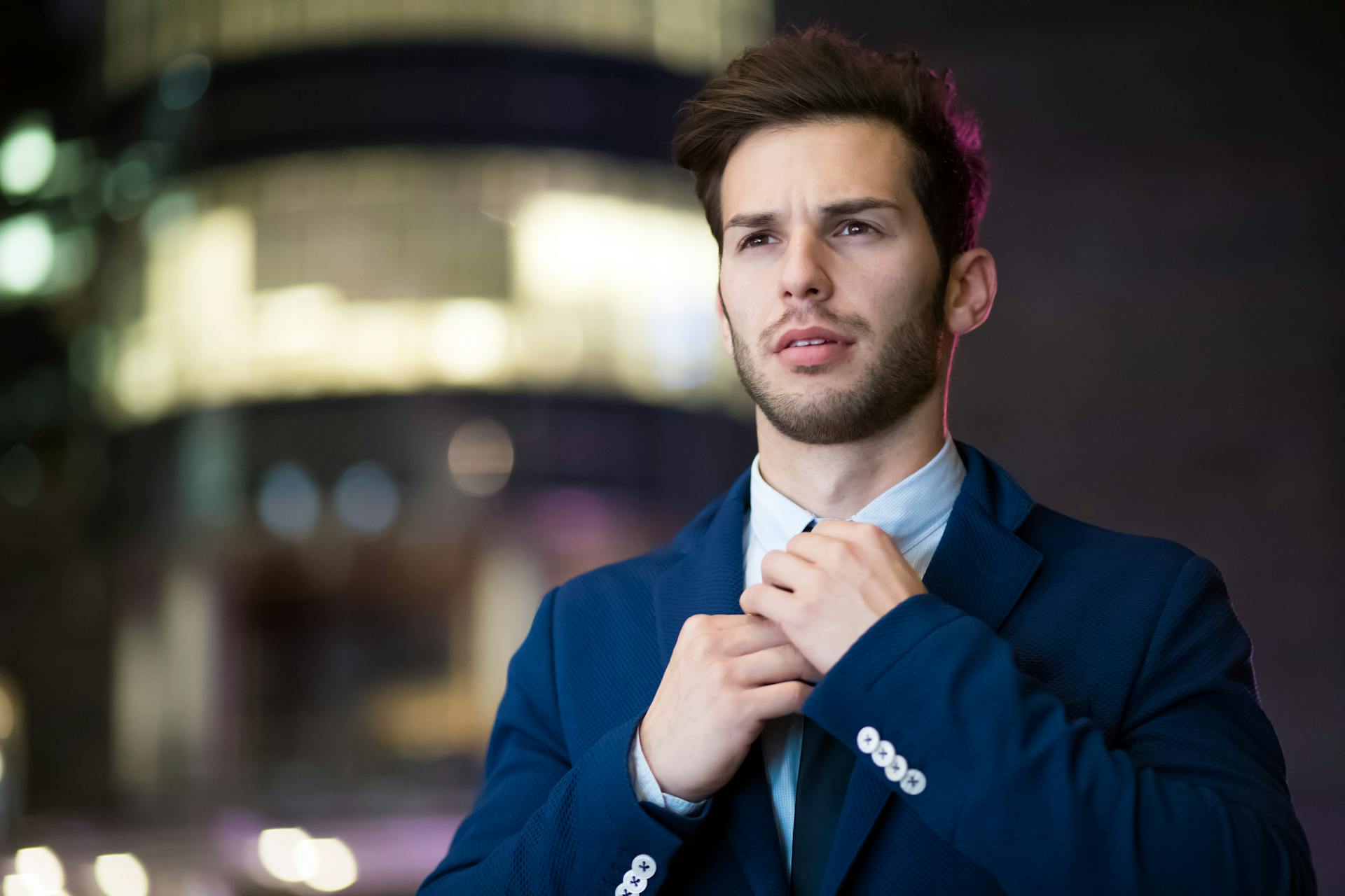 Portrait of a stylish businessman adjusting his suit in an urban night setting.