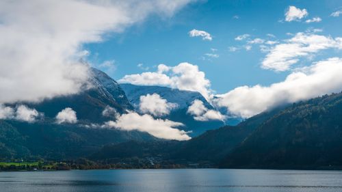 Free Serene fjord landscape featuring snow-capped mountains and low clouds under a bright blue sky. Stock Photo