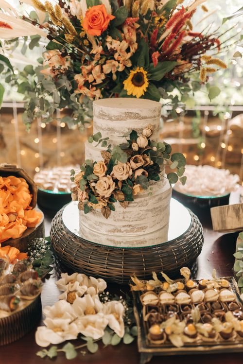 Free Elegant rustic wedding cake adorned with flowers, surrounded by an array of desserts. Stock Photo