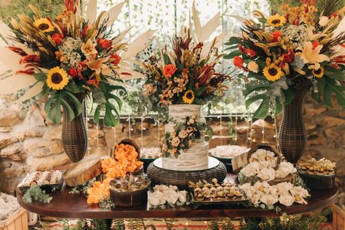 Free A beautifully decorated wedding cake surrounded by vibrant floral arrangements and confections on a rustic table. Stock Photo