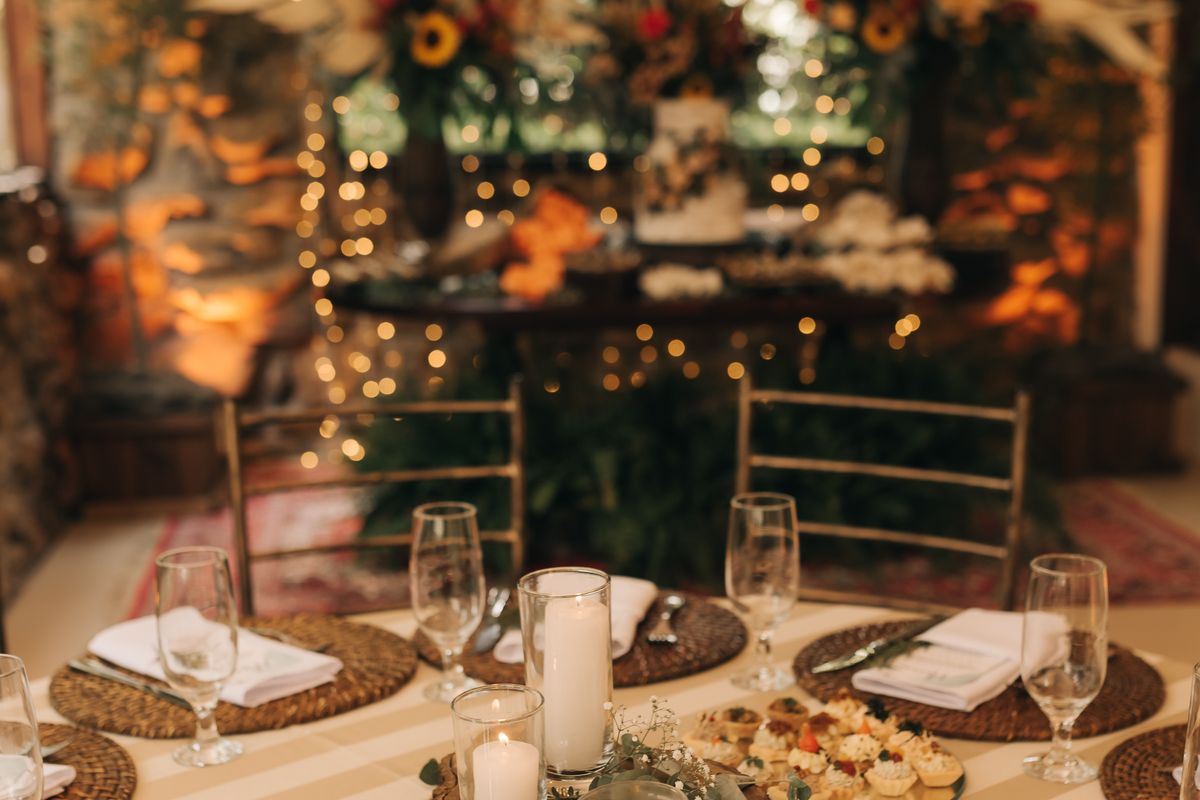 Elegant rustic fall wedding reception table with warm candlelight, string lights, and autumn floral arrangements