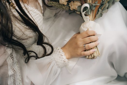Close-up of a bride's hand holding a bouquet, showcasing detailed lace on a wedding dress.