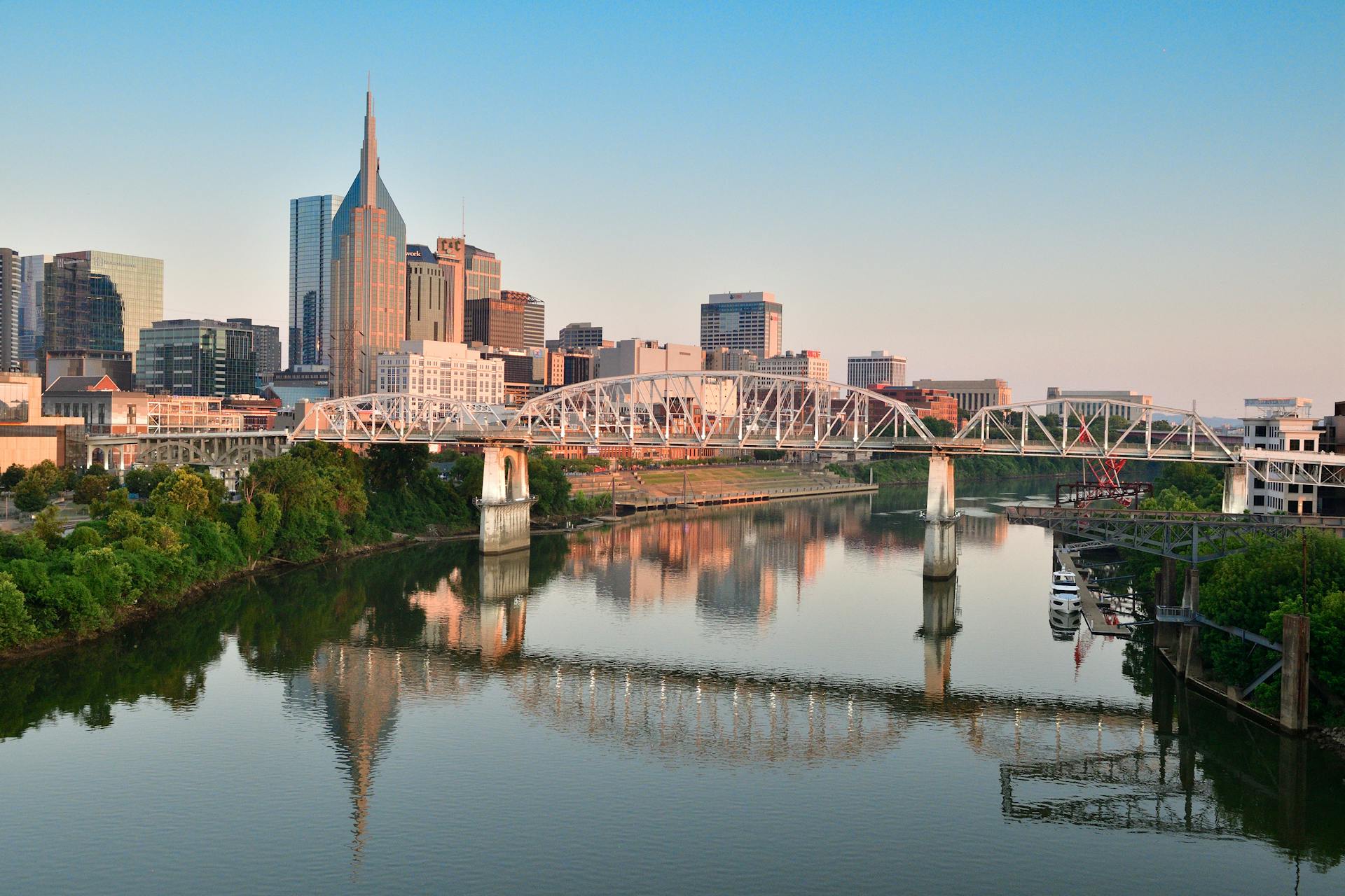 Scenic view of Nashville skyline and pedestrian bridge reflecting in the Cumberland River at sunrise.