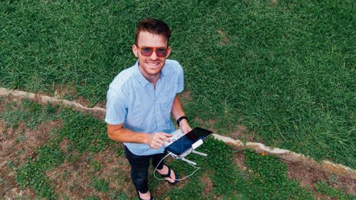 Free Top-down view of a man smiling with a drone controller in a vibrant green park. Stock Photo