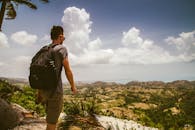 一名背着包的男性戴着太阳镜，在明亮的天空下探索广阔的山地景观