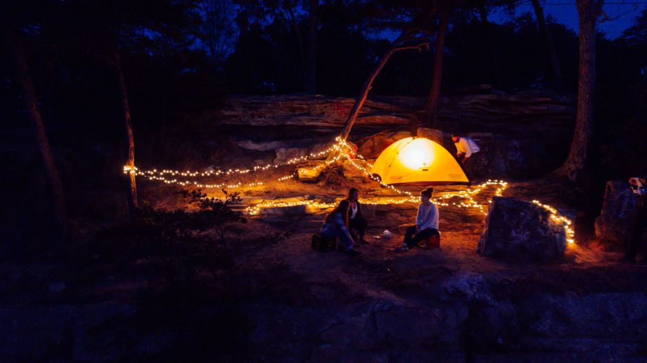 A cozy campsite illuminated by string lights and a glowing tent under a night sky.