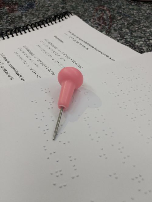 Free Braille paper with a pink stylus tool used for tactile writing by visually impaired individuals. Stock Photo