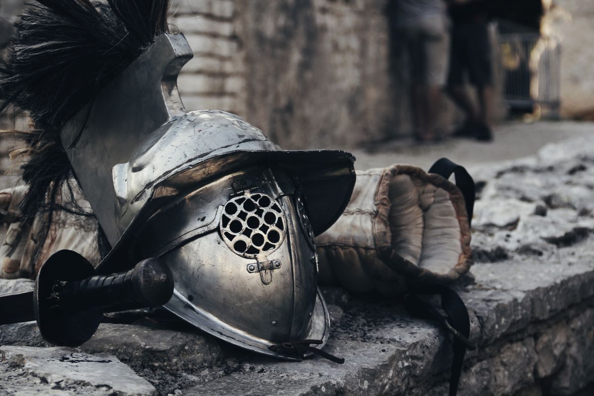Medieval helmet, sword and glove resting against a stone wall, illustrative photo