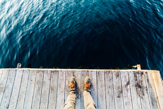 深蓝色的水面上，木码头上的人脚穿着靴子，从高角度拍摄
