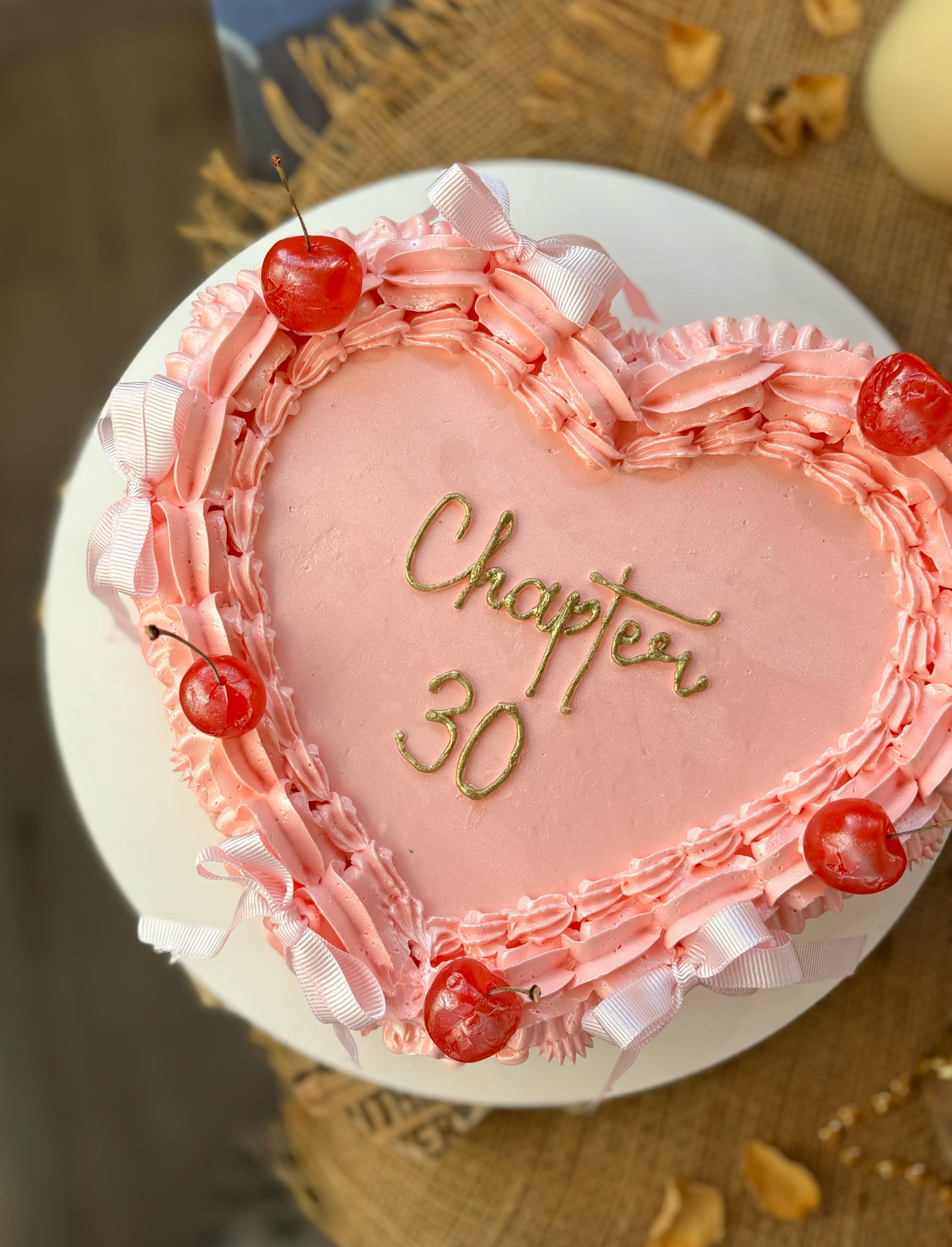 Pink heart-shaped cake with cherries and 'Chapter 30' text, perfect for celebrations.